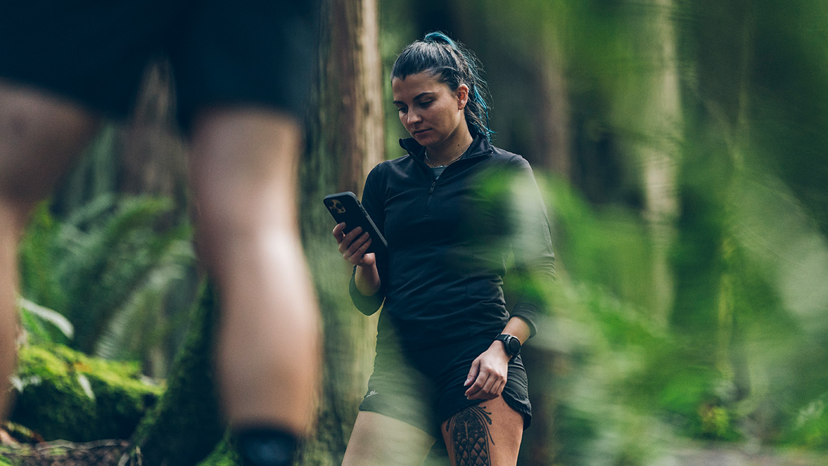 Image Of A Young Female Runner In The Woods Stopping On The Trail To Look At Her Phone To Check On Trainingpeaks Coach Payments