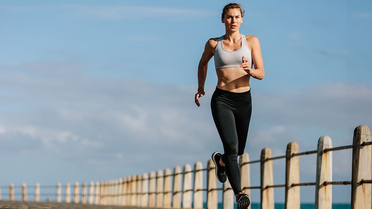 Female Runner Athlete Running Along Concrete Road In Sports Bra And Leggings.