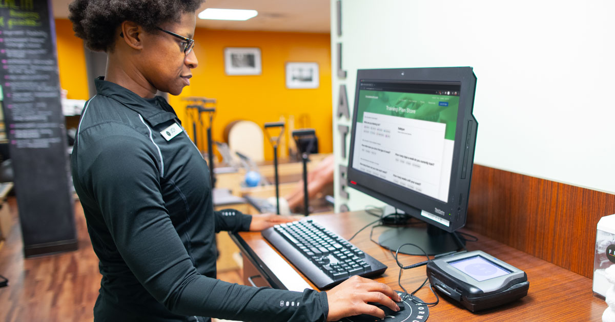 A Female Coach Working At A Desktop Computer In A Fitness Studio