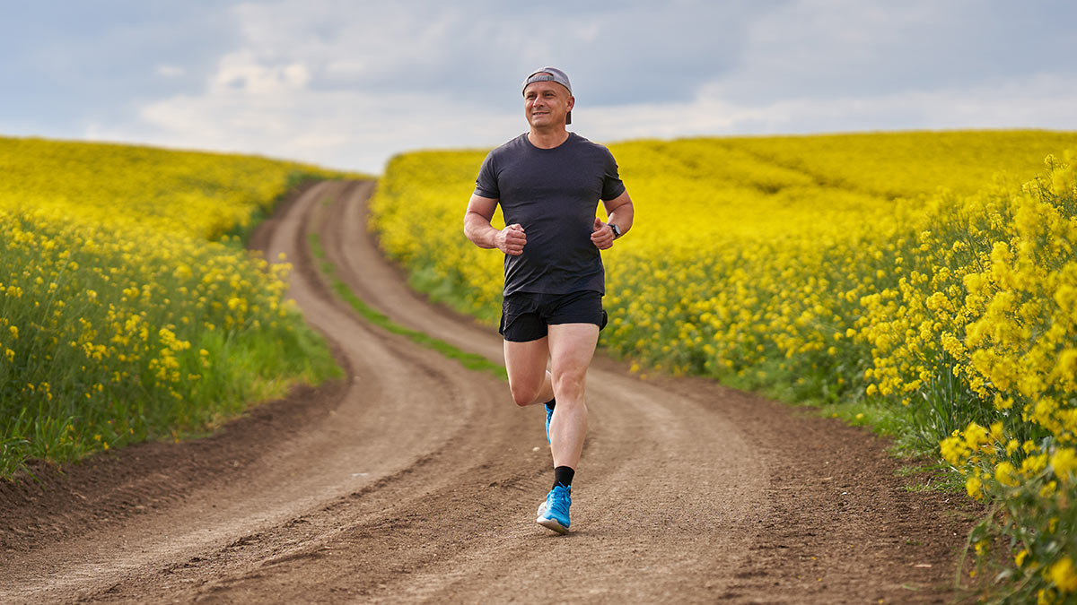 Runner Man Running Down Dirt Path In Shorts Ad Tshirt With Good Running Form On A Sunny Day