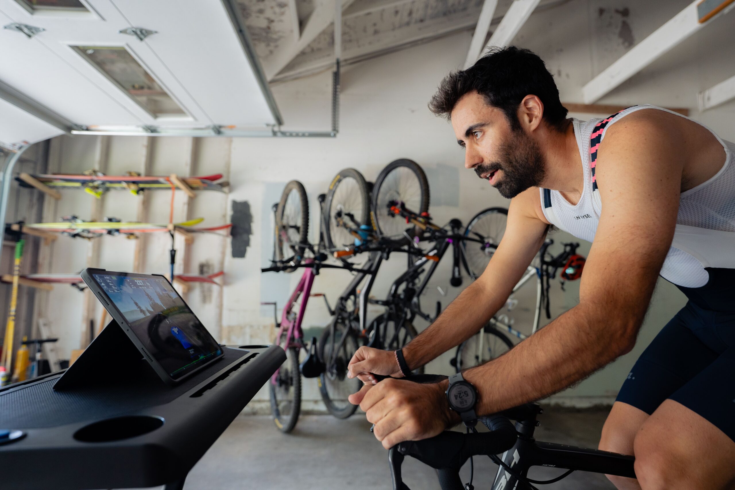Image Of A Male Cyclist Riding On An Indoor Trainer In His Garage Using Trainingpeaks Virtual With Bicycles In The Background